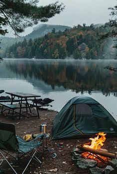 a tent is set up next to a campfire on the shore of a lake