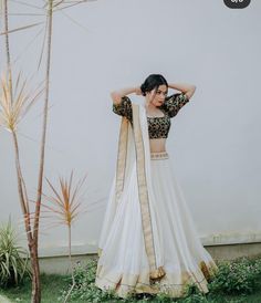 a woman in a white and gold lehenga standing next to a palm tree