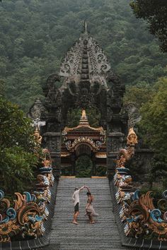 two people walking up some steps in front of a gate with an elaborate design on it