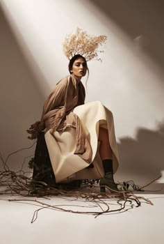 a woman sitting on top of a pile of branches holding a white bag with flowers in it