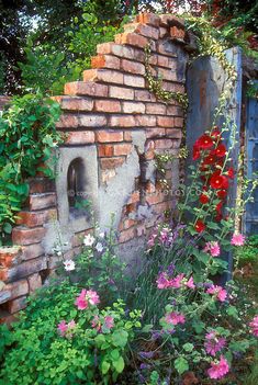 an old brick wall with flowers growing around it and a hole in the middle surrounded by greenery