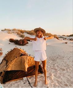 a woman standing on top of a sandy beach next to a tent in the sand