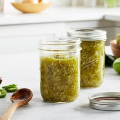 two jars filled with pickles sitting on top of a counter next to spoons