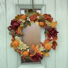 a wreath with leaves and acorns is hanging on the front door to welcome guests