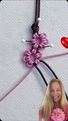 a woman holding a pink flower in front of a wall with hearts and beads on it