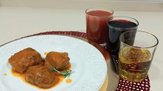 a white plate topped with meat covered in gravy next to two glasses of juice