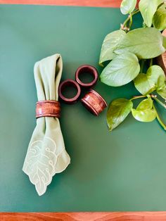 two pairs of scissors sitting on top of a table next to a green cloth and some leaves