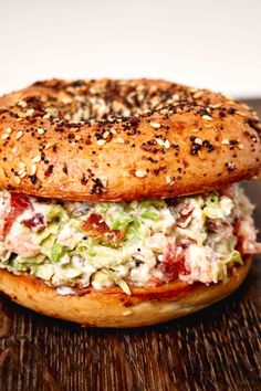 a close up of a bagel sandwich on a wooden table with sprinkled seeds