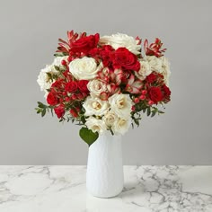 a white vase filled with red and white flowers on top of a marble countertop