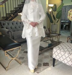 a woman standing in a living room wearing a white dress and veil over her head