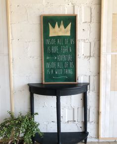 a black table with a sign on it next to a potted plant and brick wall