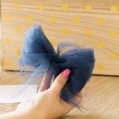 a hand holding a blue bow on top of a wooden table next to a box