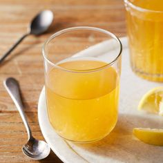 two glasses filled with orange juice on top of a white plate next to spoons