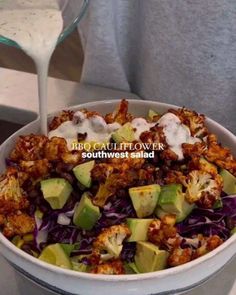 a white bowl filled with salad and dressing next to a glass of milk on a table