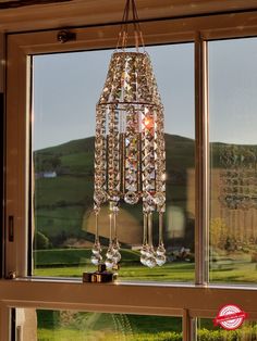 a chandelier hanging from the side of a window in front of a green hillside