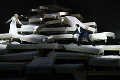 two people are walking past mattresses stacked on top of each other in a dark room