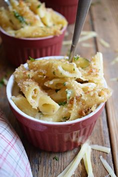 two red bowls filled with pasta and parmesan cheese on top of a wooden table