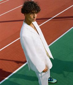 a man in a white suit standing on a tennis court with his hands behind his back