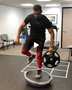 a man is doing exercises with a medicine wheel in an office setting while standing on one leg