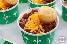 several green cups filled with chili and cornbreads on top of a football field