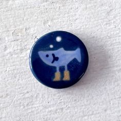 a blue button with an image of a fish on it's side, sitting on a white surface