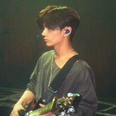 a young man holding a guitar in his right hand and wearing ear buds on his left