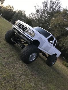 a large white truck parked on top of a grass covered field with trees in the background