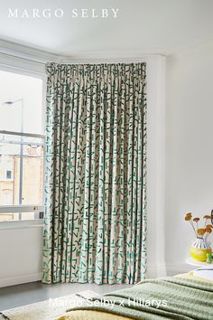 a bed sitting next to a window covered in green and white curtains with flowers on them