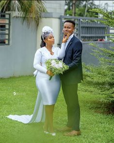 a man and woman standing next to each other in the grass with flowers on their wedding day