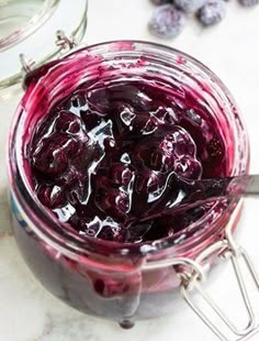 a jar filled with blueberries sitting on top of a table next to a spoon