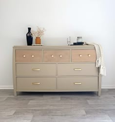 a dresser with several drawers and two vases on top of it, against a white wall