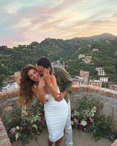 a man and woman embracing each other on top of a hill with flowers in the foreground