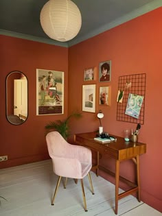 a pink chair sits in front of a desk with pictures on the wall behind it