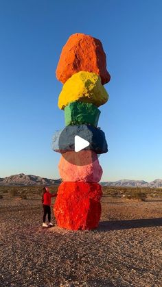 a person standing in front of a large stack of colored rocks on top of a dirt field