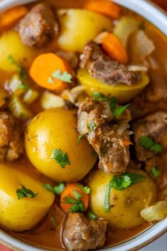 a bowl filled with stew and potatoes on top of a wooden table next to an orange napkin