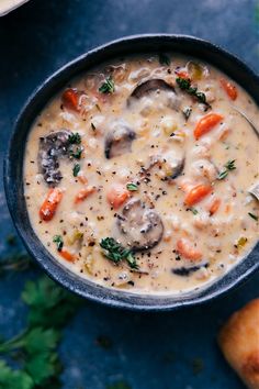 a bowl of soup with mushrooms, carrots and parsley in it on a blue surface