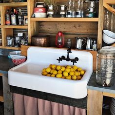 a white sink sitting in the middle of a kitchen next to a wooden shelf filled with dishes