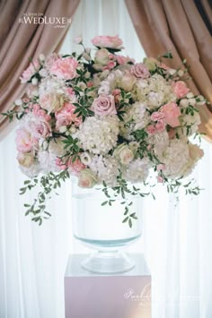 a vase filled with pink and white flowers on top of a table next to a window