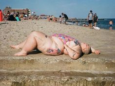 a man laying on top of a sandy beach next to the ocean with people in the background