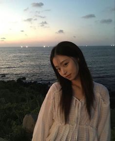 a woman standing in front of the ocean at sunset