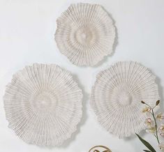 three white wicker plates on a table next to a vase with flowers in it