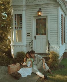 a man and woman sitting on the ground in front of a house with their luggage