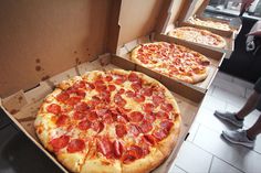 two pizzas sitting on top of cardboard boxes next to each other, one with pepperoni and the other with cheese