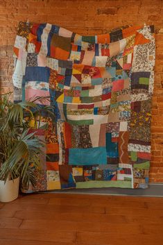 a large multicolored patchwork quilt hanging on a brick wall next to a potted plant