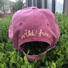 a pink hat with the words wild and free on it sitting in some green bushes