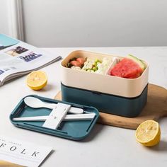 a bento box filled with food on top of a cutting board next to sliced lemons