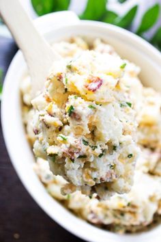 a white bowl filled with potato salad on top of a wooden table next to green leaves