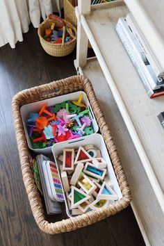 a basket filled with lots of toys on top of a wooden floor next to a window