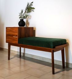 a wooden bench with a green cushion on it next to a plant in a black vase