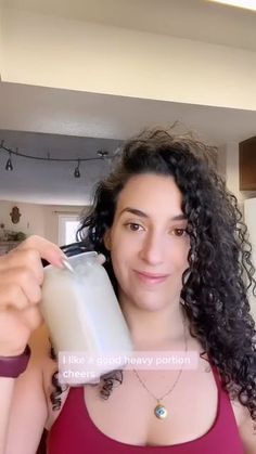 a woman in a red tank top is holding a milk bottle and looking at the camera